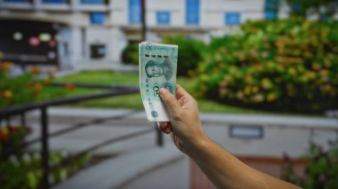 Şehir parkı ortamında Çin Yuan banknotunu elinde tutan adam, şehir yaşamındaki dolandırıcılığı sembolize ederek para ve ekonomiye odaklanıyor..