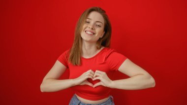 Kırmızı arka planda izole edilmiş, elleri sırıtan, kalp şeklinde genç bir kadın.