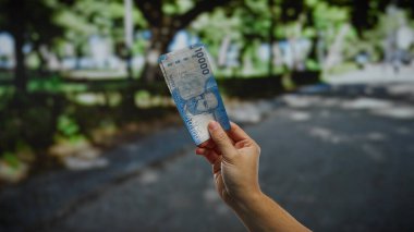 Güneşli bir sokakta elinde Şili pezosu olan bir adamın şehir ortamındaki yatırımları ve finansal işlemleri sembolize eden fotoğrafı..