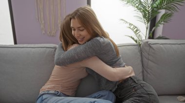 Kapalı bir yerde kanepede kucaklaşan kadınlar, rahat oturma odası ortamında kardeşçe sevgi ve aile bağlarını gösteriyor, yakınlığı, sıcaklığı ve aile hayatının mutluluğunu vurguluyorlar..