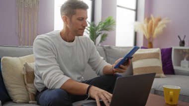 Genç adam rahat oturma odasında dizüstü bilgisayar ve kahveyle rahat ve modern bir yaşam tarzını bitkilerle ve şık dekorlarla ön plana çıkarıyor..