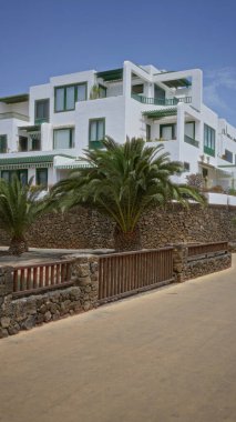 Gündüz vakti, Lanzarote, kanarya adalarında açık mavi gökyüzüne karşı kurulmuş palmiye ağaçları ve taş duvarlarla çevrili modern beyaz apartman kompleksi..