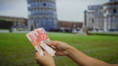 Pisa, İtalya 'nın eğimli kulesinin önünde Hong Kong dolarlarını tutan adam, açık hava manzarası tasvir ederek para, yatırım ve seyahat yönlerini ön plana çıkarıyor..