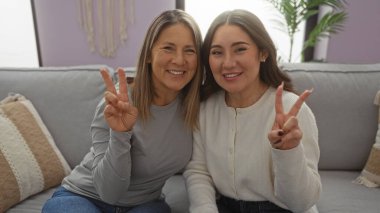 Anne ve kızı, kapalı bir İspanyol aile evinde rahat bir kanepede otururken barış işareti yapıyorlar..