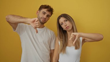 Sarı arka planda baş parmak gösteren erkek ve kadın hayal kırıklığına uğramış ve ciddi görünüyorlar. Onaylamadıklarını ifade ediyorlar. Diğerlerinden soyutlanmışlar..