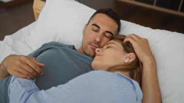 Kadın ve erkek rahat bir yatak odasında birlikte uyur, sıcak bir yuva ortamında birbirini sevgiyle kucaklar, mahremiyet ve sükuneti yansıtır..