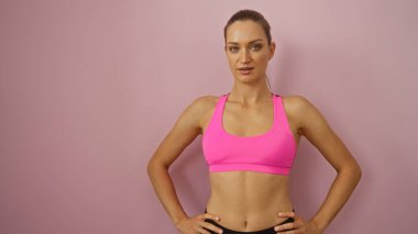 Yumuşak pembe arka planda poz veren, canlı pembe bir spor bluzu giyen kadın tenha modern ve minimalist estetik figürlerini sergiliyor..