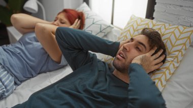 Yatak odasındaki kadın ve erkek kulaklarını kapatıyor, evde hayal kırıklıklarını ifade ediyorlar, ilişki zorluklarını vurguluyorlar ve duygularını paylaşıyorlar..