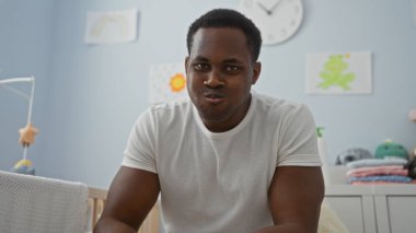 Yatak odasındaki yakışıklı genç adam bebek beşiğinin yanında gülümsüyor. Sıcak ve davetkar bir atmosfer yaratıyor. Etrafını pastel renkler sarıyor..