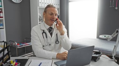 Klinikteki doktor masada ve laptopta steteskopla konuşuyor, profesyonel sağlık hizmetleri atmosferini aktarıyor..