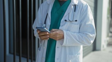 Beyaz önlüklü doktor hastanenin dışında akıllı telefon tutuyor. Şehir ortamındaki teknolojiyi kullanarak tıbbi profesyonelleri gösteriyor..