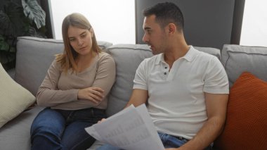 Kanepede oturan erkek ve kadın rahat bir oturma odasında belgeleri tartışıyor, rahat bir evde samimi bir ilişki sergiliyorlar..