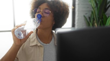 Kıvırcık saçlı ve gözlüklü bir ofiste su içen kadın, işyerindeki su kaybına ve ev içi rahatlığına odaklanıyor..
