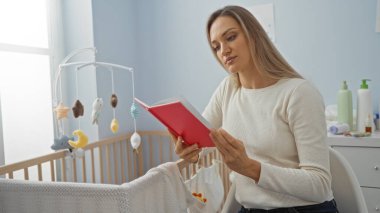 Bebek beşiğinin yanında kitap okuyan kadın, rahat yatak odasında, bebek odası oyuncakları, gündüz ışığı ve huzurlu ev atmosferiyle huzurlu iç mekan sahnesini anlatıyor..