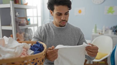 Genç İspanyol bir adam çamaşırhanede temiz giysileri sınıflandırıyor. Düzenli bir şekilde ev işlerine odaklanmış ev işlerini gösteriyor..