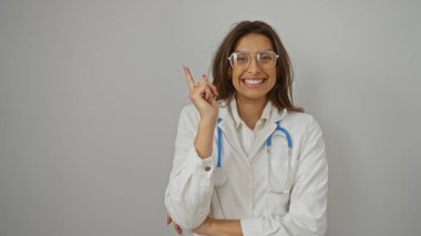 İzole edilmiş beyaz bir arka plan duvarının üzerinden yan bakan kadın doktor pozitifliğini ve profesyonelliğini ifade ediyor gözlük ve steteskop takıyor..
