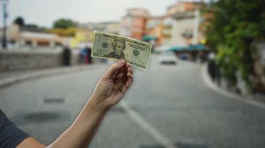 Şehir caddesinde elinde Amerikan Doları banknotları tutan adam, açık bir şehir ortamında döviz değişimi sergiliyor..