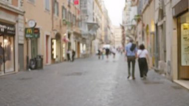 Roma 'da, bulutlu bir günde tarihi binalar ve dükkanlarla dolu kaldırım taşlarında yürüyen bulanık yayaların olduğu odak dışı sokak sahnesi..