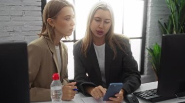 İş kadınları bir ofis ortamında birlikte çalışırlar, bilgisayarın yanında işle ilgili görevleri tartışırken akıllı telefona odaklanırlar..