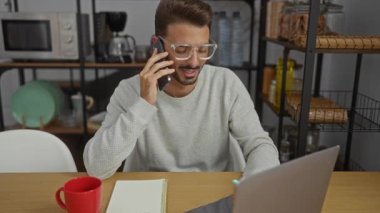 Ofiste çalışan İspanyol gözlüklü adam telefonla konuşuyor. Etrafı defter, kahve fincanı ve dizüstü bilgisayarla çevrili. Modern bir iş ortamında verimliliği somutlaştırıyor..