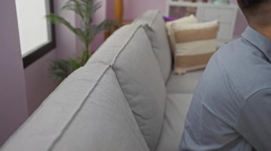 Rahat bir oturma odasındaki kanepede dinlenen genç bir adam. Etrafında yumuşak yastıklar, sakin bir iç mekanda yakalandı..