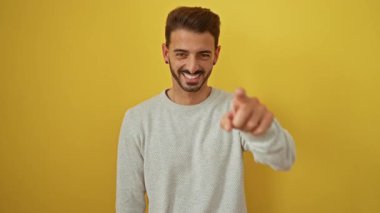 Genç İspanyol asıllı adam kameraya doğru gülümsüyor ve canlı sarı bir arka plana karşı özgüven ve cazibeyle, modern pozitifliği ve gençlik enerjisini somutlaştırıyor..