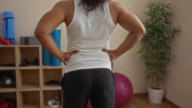 Sırt ağrısı olan genç bir adam egzersiz ekipmanları ve bitkilerle çevrili bir sağlık odasında dinlenme ve terapi için sakin bir spa atmosferini vurguluyor..