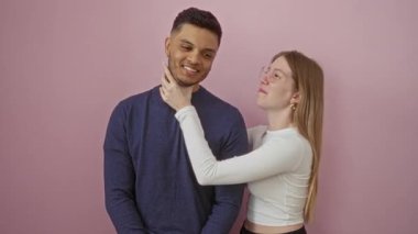 Çift pembe duvara karşı oynak bir anı paylaşıyor erkeğin boynunu nazikçe tutan, içten gülümseyen, sevgi dolu bir bağ ve samimi bir ortamda gerçek bir sevgi ifade eden bir kadınla..