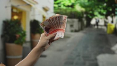 Bir şehir caddesinde Norveç kronunu elinde tutan adam, canlı bir açık hava ortamında para gösteriyor, ekonomik temaları ve kişisel finans bağlamını vurguluyor..