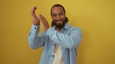 Parlak sarı bir duvara gülümseyen ve alkışlayan bir adam, açık mavi bir gömlek giyen, neşeli ve neşeli bir ortamda neşe ve pozitifliği tasvir eden, reklam amaçları için mükemmel..