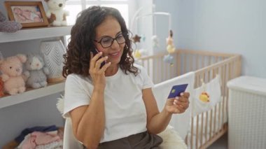 Telefondan konuşan bir kadın, kapalı bir odada kartıyla oturuyor. Beşiğin yanında. Etrafı lüks oyuncaklarla çevrili..