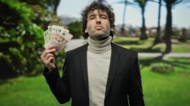 Parktaki Arjantinli adam, yeşilliklerle çevriliyken jestleri vurguluyor..