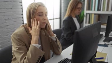 Bilgisayarlı bir ofiste çalışan, yorgunluk ve stresi ifade eden iki profesyonel sarışın kadınla modern bir iş ortamı sergileyen kadınlar..