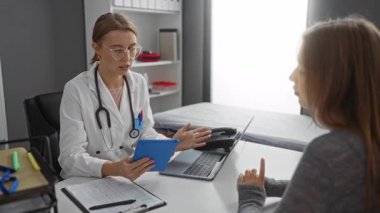 Tıbbi araçlarla çevrili klinik odasında doktor danışmanı hasta, iki kadının profesyonel iç mekan ortamında sağlık hizmeti sunuyor.