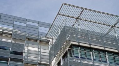 Açık mavi gökyüzüne karşı güneş ışığını yansıtan açısal metal yapılara sahip cam cepheli modern mimari çağdaş kentsel tasarım ve yenilik sergiliyor..