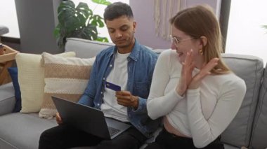 Evdeki çift online alışverişi kartla kutluyor, dizüstü bilgisayarlı bir adam ve sıcak oturma odasında neşeyle sarılan bir kadın..