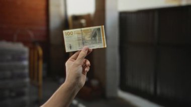 Bir inşaat sahasında Danimarka kronu banknotları tutan bir adam, doğal ışıklandırma ile bir ev yenileme ortamında para vurguluyor..