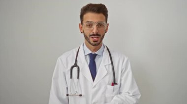 Gözlüklü ve steteskoplu bir doktor beyaz arka planda sessizlik için jestler yaparak gizlilik ve profesyonelliği vurguluyor..