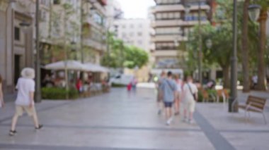 Bulanık sokak manzarası. Binalar, ağaçlar, yürüyen insanlar ve güneşli şehir ortamında açık hava kafeleri.