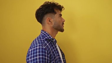 Ekose gömlek giyen sakallı genç adam canlı sarı bir arka plan, somut bir stil ve karizmaya karşı özgüvenli görünüyor..