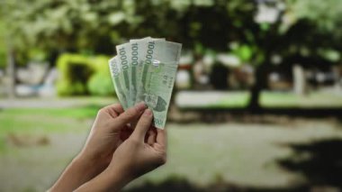 Güney Kore 'yi elinde tutan adam bir parkta banknotlar kazandı, açık havada, yemyeşil bir arka bahçeye karşı para sergiliyordu..
