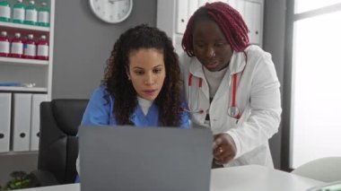 İki kadın doktor, bir hastane kliniğinde dizüstü bilgisayarla iş birliği yapıyor. Tıbbi bir ortamda takım çalışması ve kendini işine adamış..