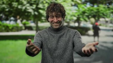 Arka planda ağaçlarla parka davet eden İspanyol genç adam güneşli bir günde dostça ve misafirperver bir jest yapıyor.