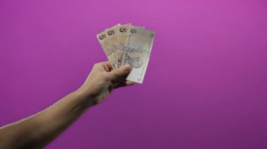 Canlı mor bir duvara karşı Türk lirası banknotları tutan adam, modern izole edilmiş bir ortamda finansal konseptler ve para değişimi sergiliyor..