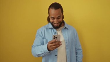 Akıllı telefonu parlak sarı arka planda tutan bir adam gülümseyen modern teknoloji portresi kendinden emin ifadeyi baş parmağında oynatıyor.