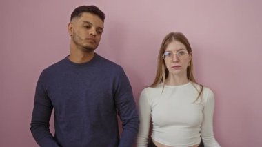 Kadın ve erkek, pembe bir arka plan karşısında baş parmağıyla onaylamayan hareketler yaparak, izole bir ortamda bir çiftin ortak memnuniyetsizliğini vurguluyor..