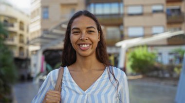 Şehir parkında gülümseyen genç bir kadın, güzel ve mutlu bir Afro-Amerikalı 'yı, ışıl ışıl yüzüyle gösteriyor..