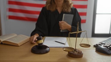 Yargıç kadın, elinde arka planda Amerikan bayrağı olan bir kitapla mahkeme salonunda oturmuş tokmak ve adalet terazisi gibi hukuki semboller sergiliyor.