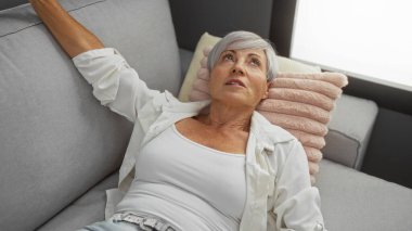 Güzel, yaşlı bir kadın. Kısa gri saçlı. Oturma odasındaki kanepede dinleniyor..