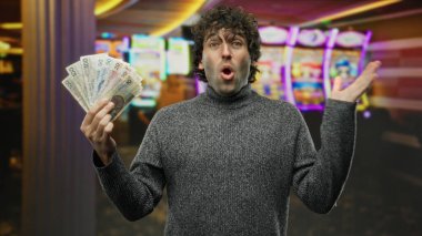İspanyol asıllı bir adam kumarhanenin içinde kumar makineleri olan bir kumarhanede para tutuyor, heyecan ve şaşkınlık ifade ediyor, canlı ışıklar ve oyun atmosferiyle çevrili..